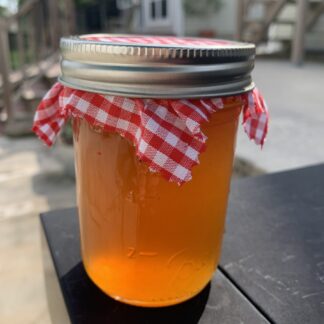 A glass jar of apple cider jelly appears to glow amber in color in the morning sunshine.