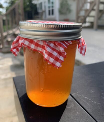 A glass jar of apple cider jelly appears to glow amber in color in the morning sunshine.