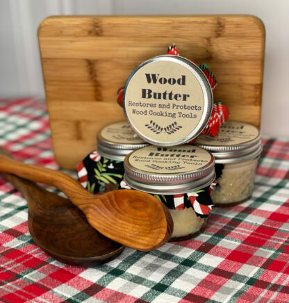 Small jars of wood butter sit stacked up beside two wooden spoons and a wood cutting board.